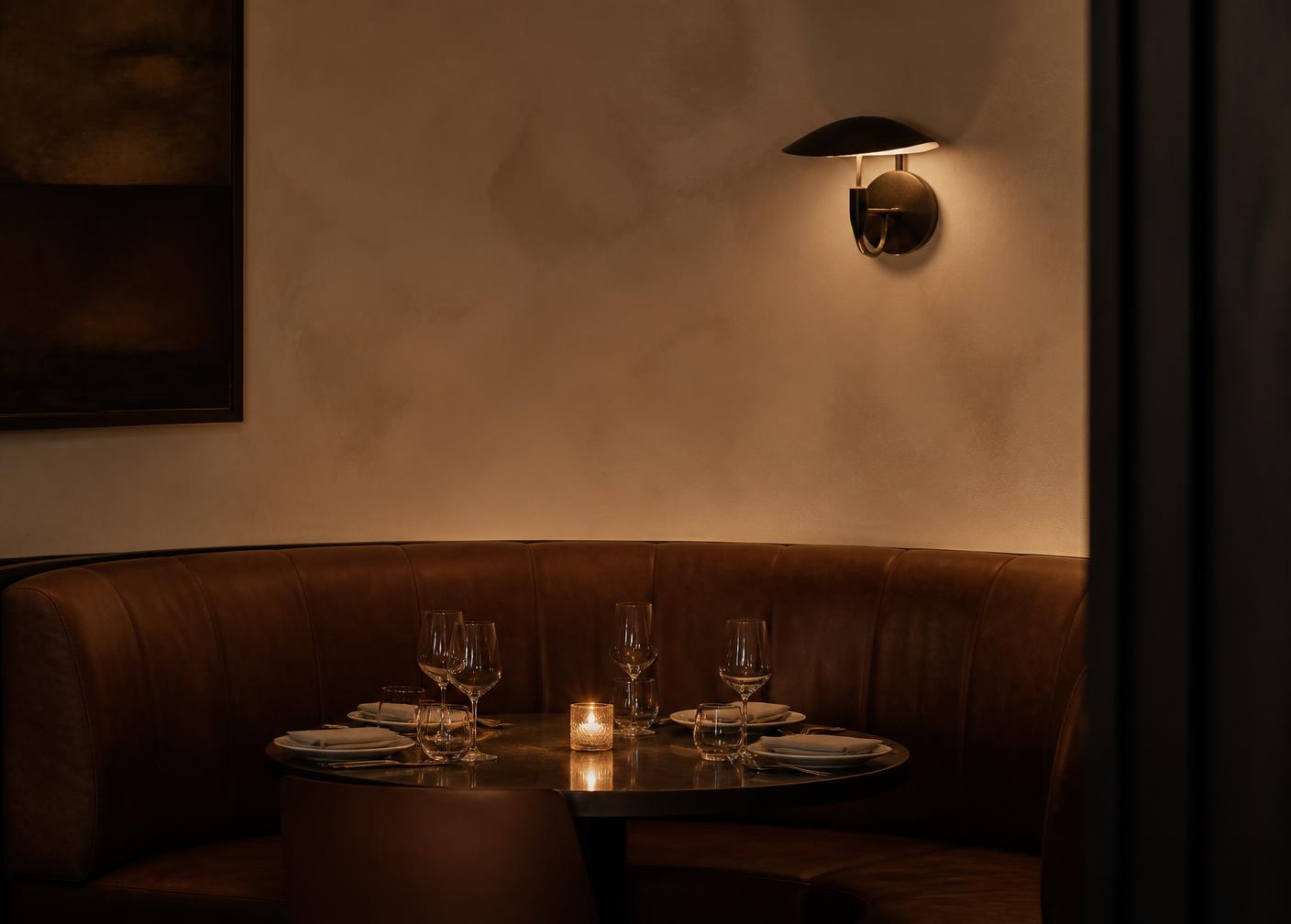 Curved leather banquette set for dinner under a warm brass sconce