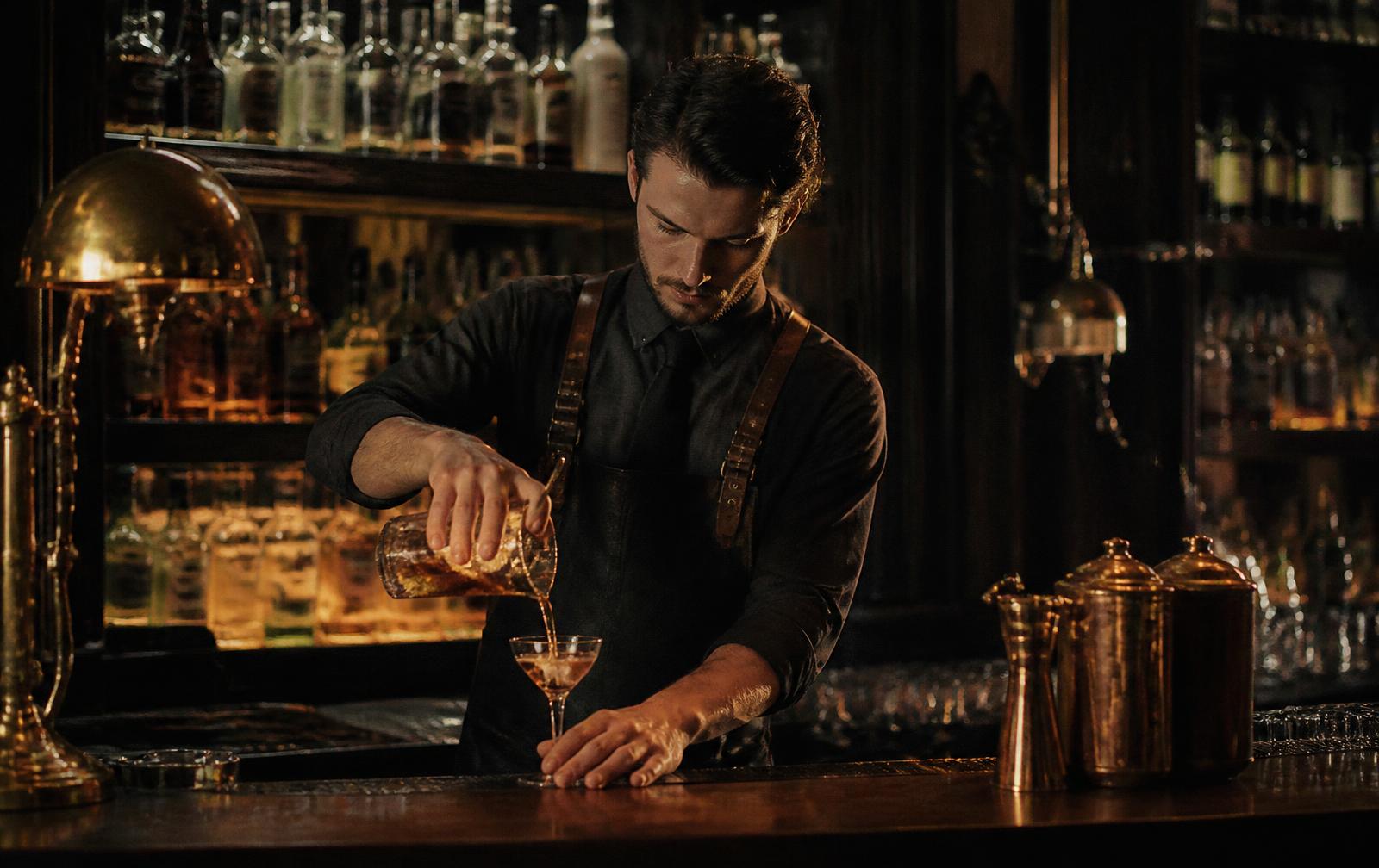 Bartender pouring a cocktail behind the dark brass-lit VÉRA bar