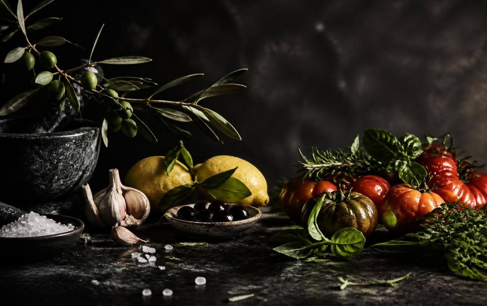 Mediterranean ingredients including olives, lemons and herbs on dark stone