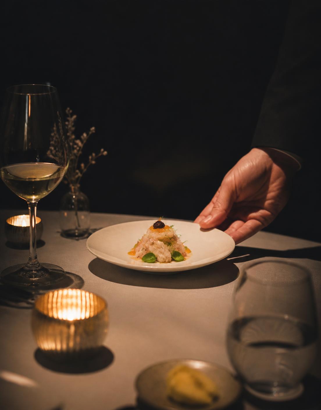 A delicate tasting menu course being placed on a candlelit table